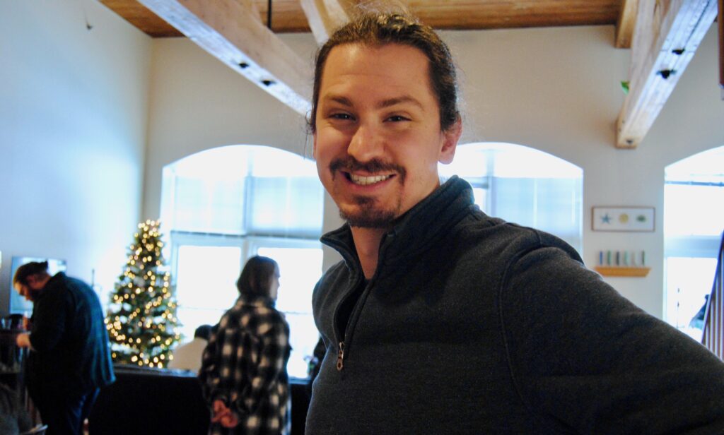 A picture of a brown-haired man with a goatee, smiling at what appears to be a holiday party.